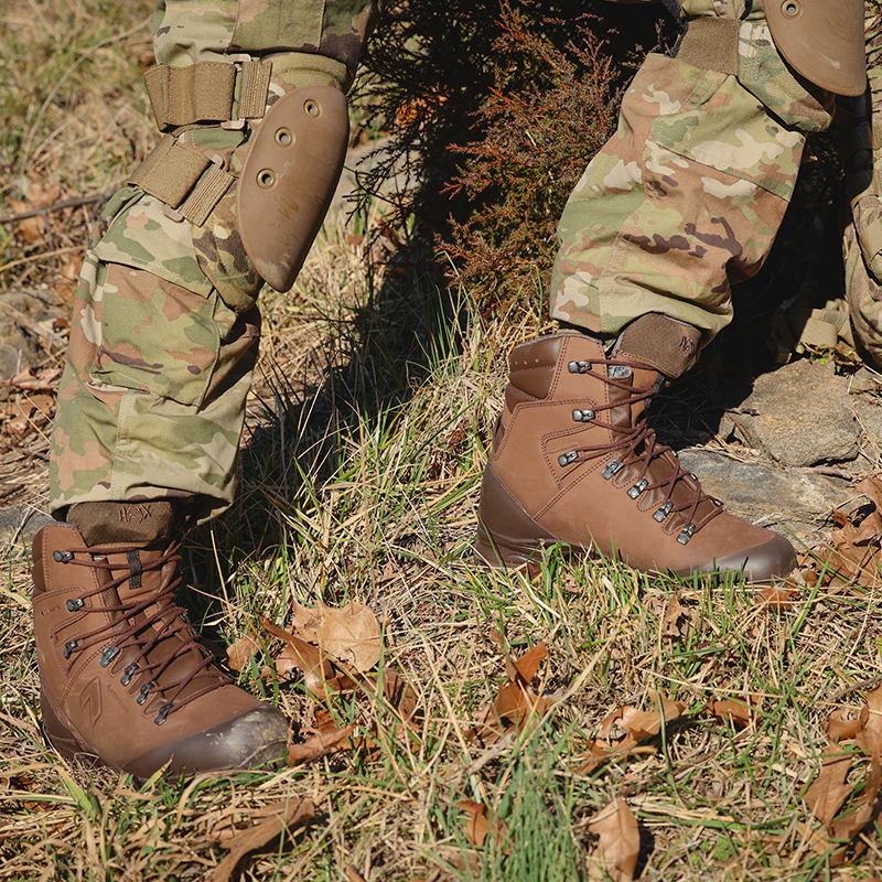 Close up of dark brown Combat Forge boots worn with OCP pants and knee guards, standing on uneven, grassy terrain